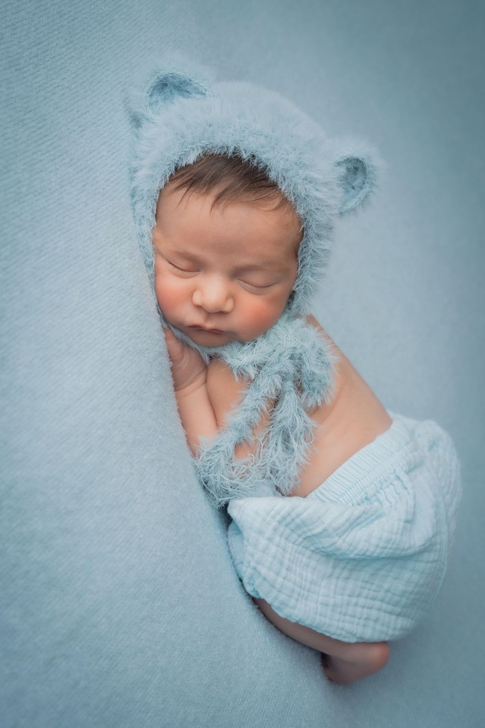 Neonato con il cappellino a orsetto su fondo azzurro